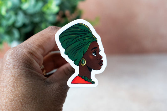 Sticker of a person with a green headscarf held by a hand with a blurred background